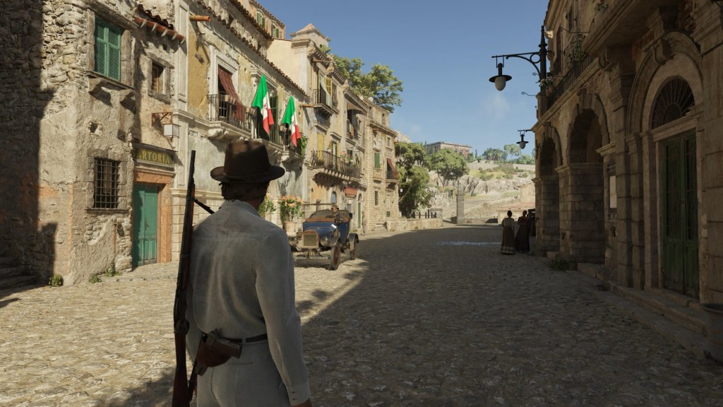 A sunlit Sicilian village street with stone buildings and Italian flags in Mafia: The Old Country